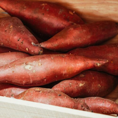 Close-up of fresh sweet potatoes in a wooden crate, ideal for cooking.