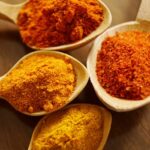 Close-up of vibrant spices like turmeric and chili powder in wooden spoons.